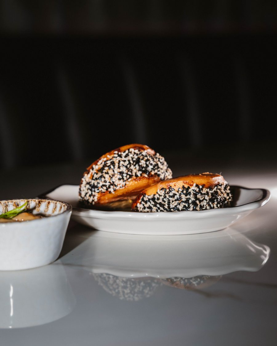 Sesame-crusted golden buns on a white plate with a small dish of sauce
