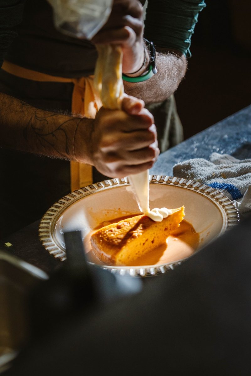 A chef piping cream onto a slice of cake in a shallow bowl